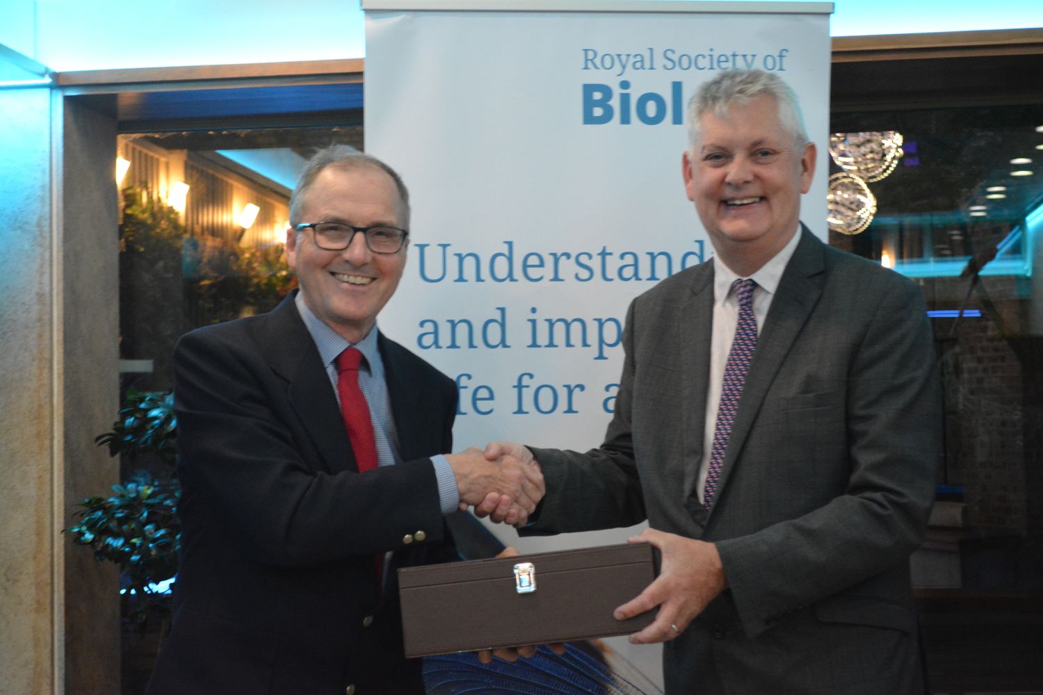 Ian Boyd shaking hands with Mark Downs and handing over bottle of wine in front of RSB banner